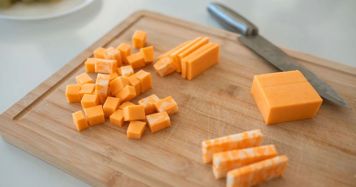 Cubes and sticks of cheddar cheese on a wooden board