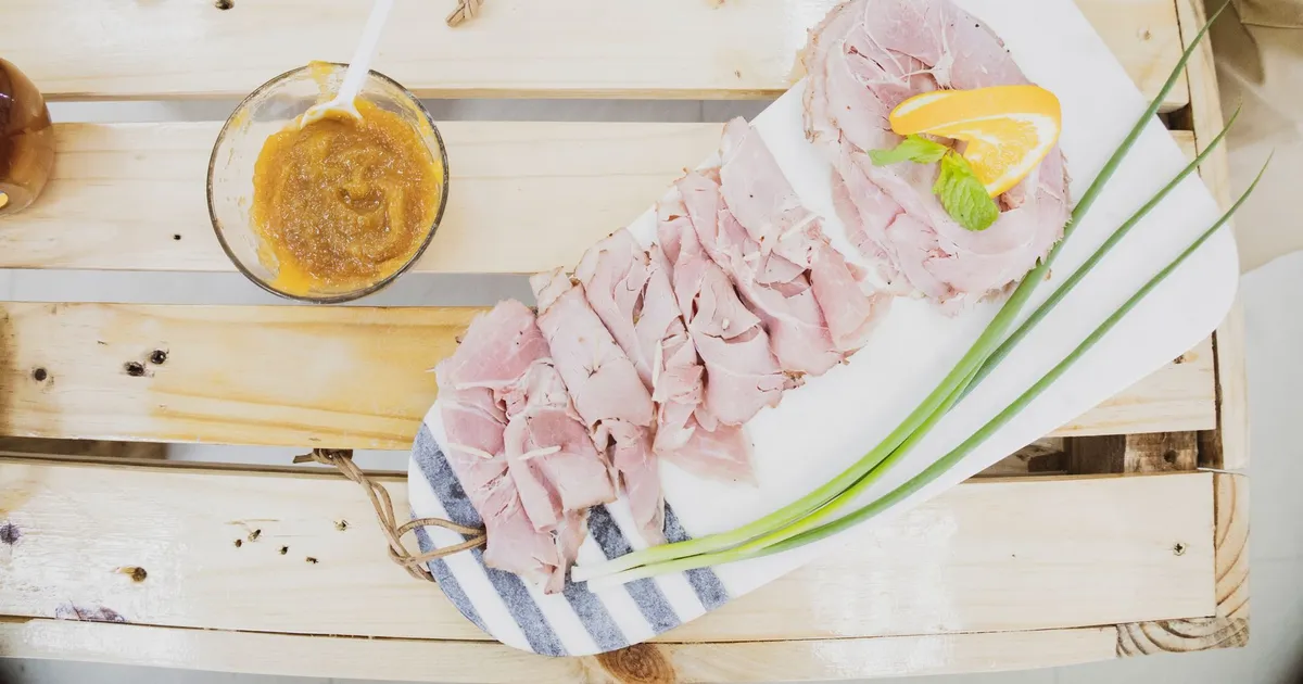 Slices of ham on a board with mustard and chives