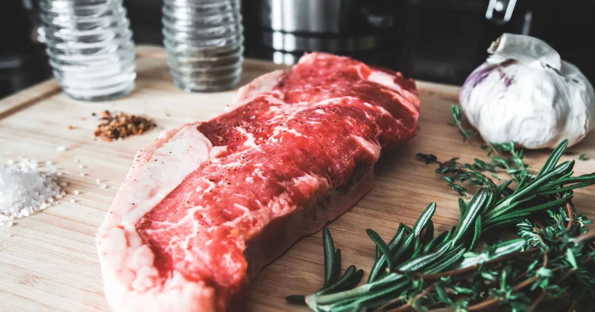 Raw beef steak on a wooden board with rosemary and garlic